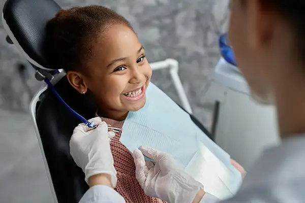 A smiling girl sitting in the dentist chair while a hygienist prepares them for their dental visit.