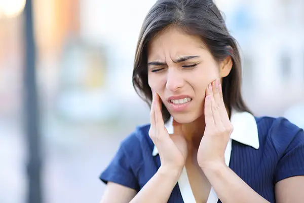 A woman grasping her jaw with both hands in pain